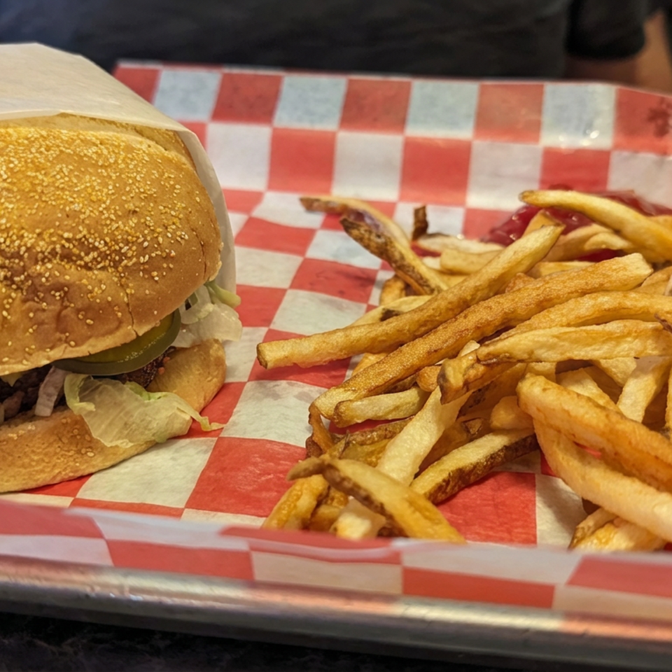 Cheeseburger with lettuce and pickles served alongside golden fries on a red-and-white checkered tray liner.
